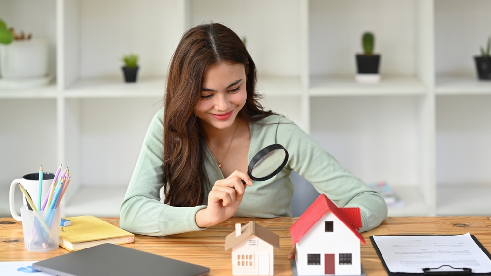 Smiling,female,appraiser,looking,at,house,model,through,magnifying,glass.